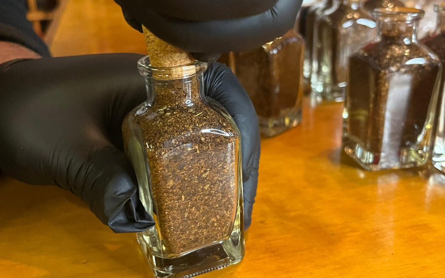 Manos con guantes envasando merkén a mano en una botella de vidrio con corcho