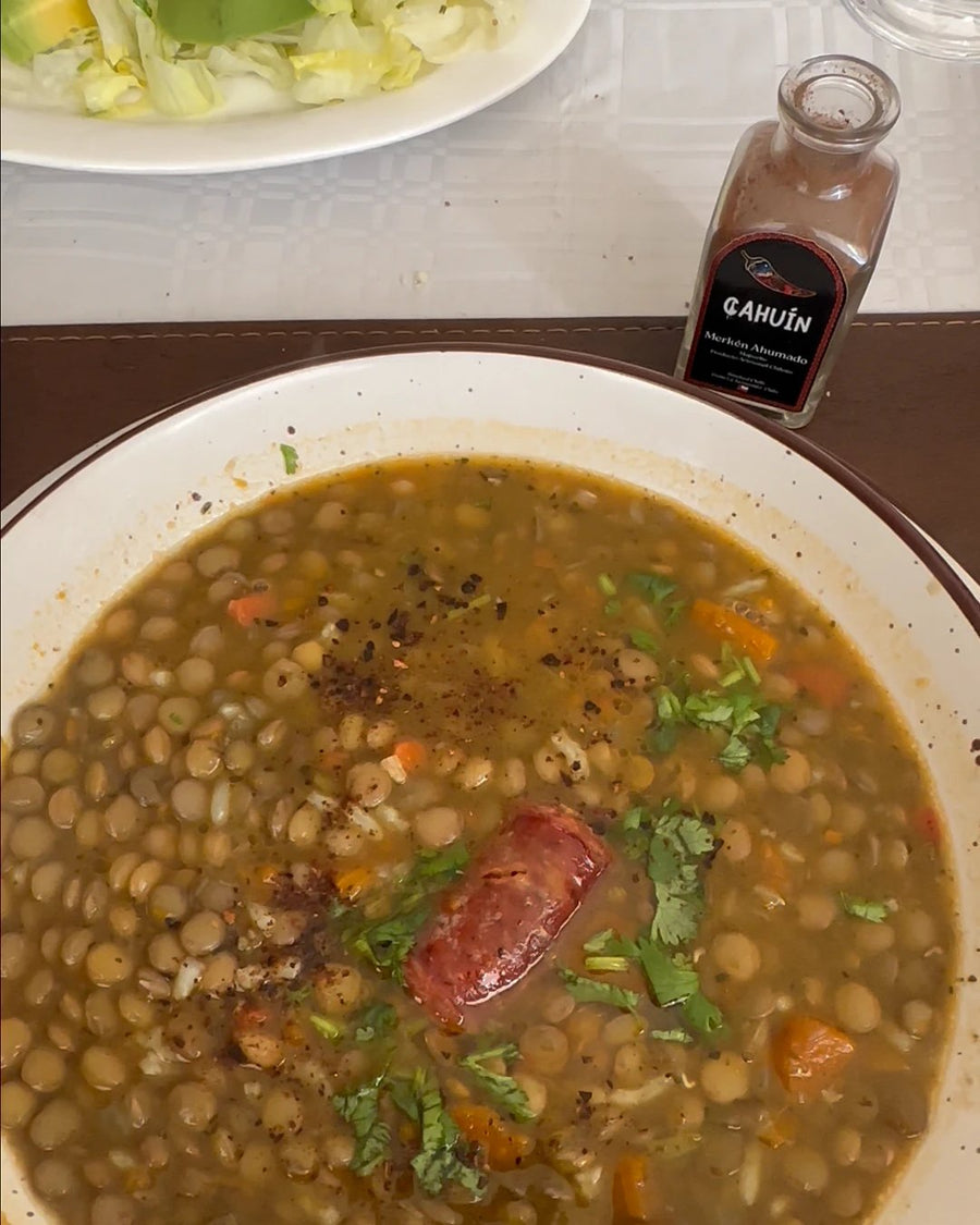 Plato de lentejas con merkén espolvoreado y una botella de MERKÉN CAHUÍN al lado